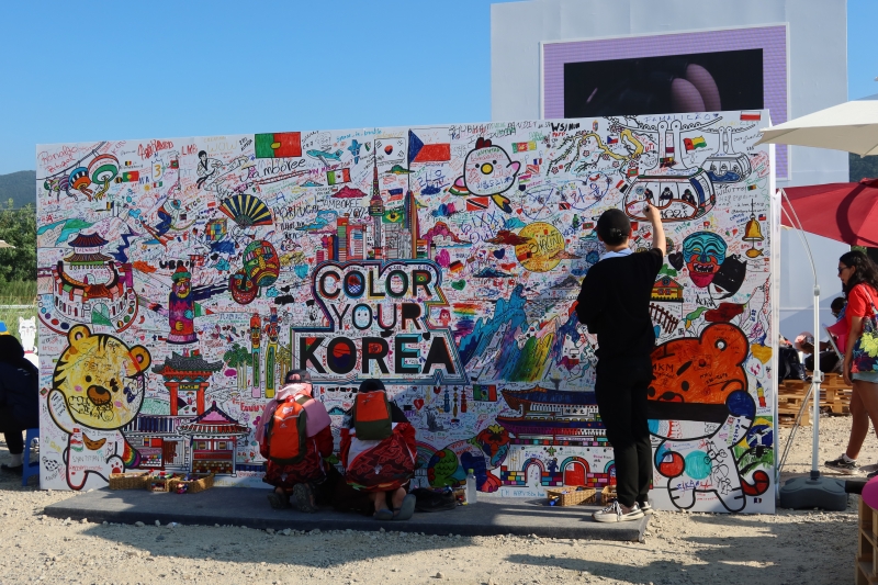 Scouts and visitors at the 25th World Scout Jamboree in Saemangeum on Aug. 5 write and draw on a coloring wall with Korean tourist landmarks set up by the Korea Tourism Organization at the entrance of the campsite.Inscribed with the phrase 