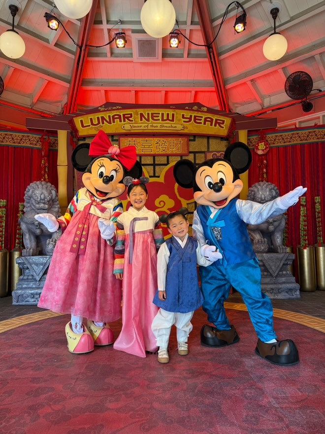 A screenshot from an Instagram Reel shared by Catherine Eum showing her kids, Emily and Elias, wearing matching Hanboks with Mickey and Minnie Mouse at Paradise Gardens in Disney California Adventure Park. (Catherine Eum)